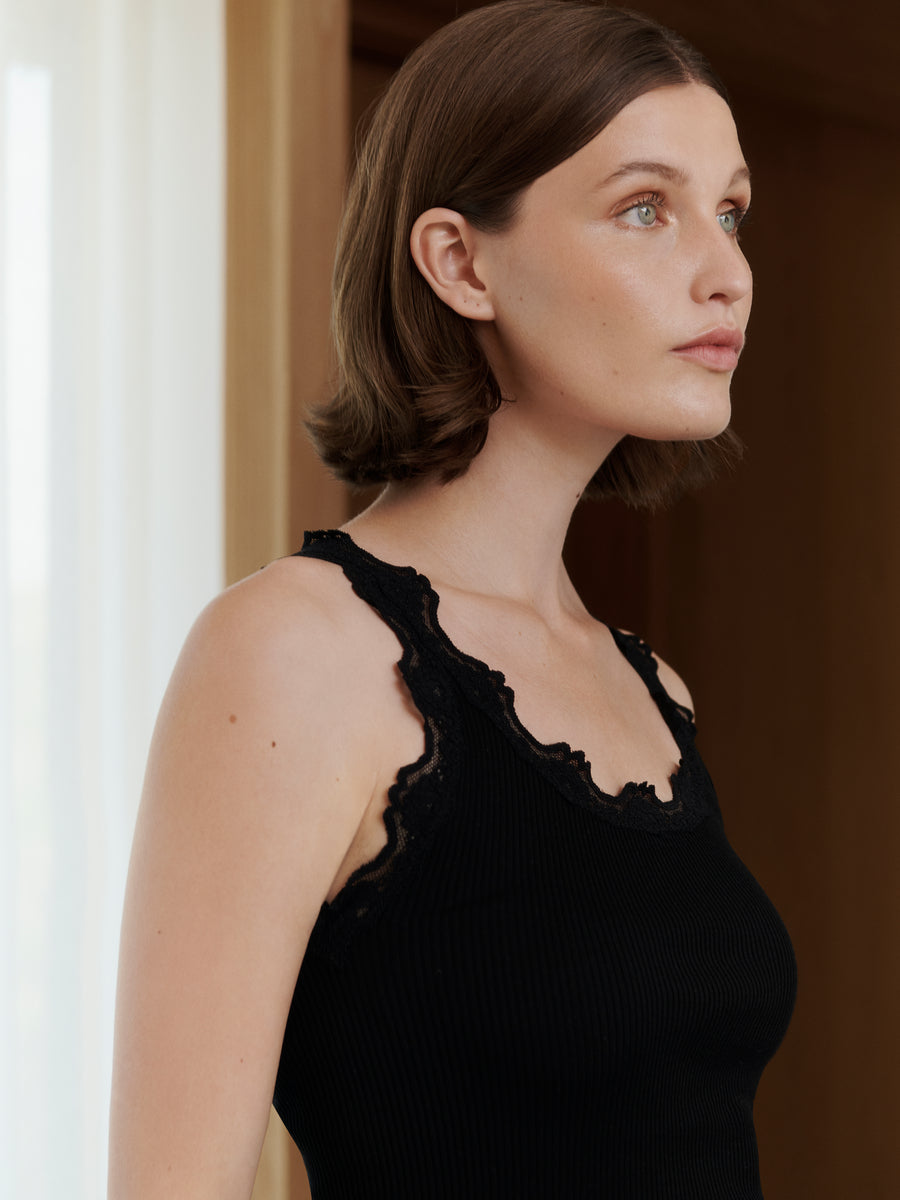 Woman wearing a black sleeveless top with lace details, standing indoors.